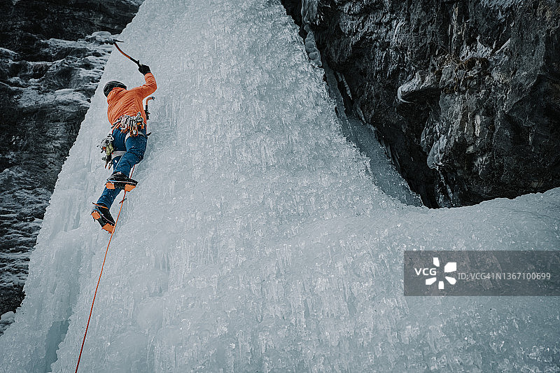 男性攀冰者挥舞冰镐攀登高大冰冻瀑布的仰视角度照片图片素材