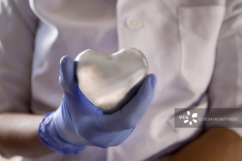 戴蓝色外科手套，手持银色爱心的黑人女医护人员图片素材