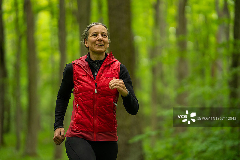 微笑的中年妇女在森林中慢跑图片素材