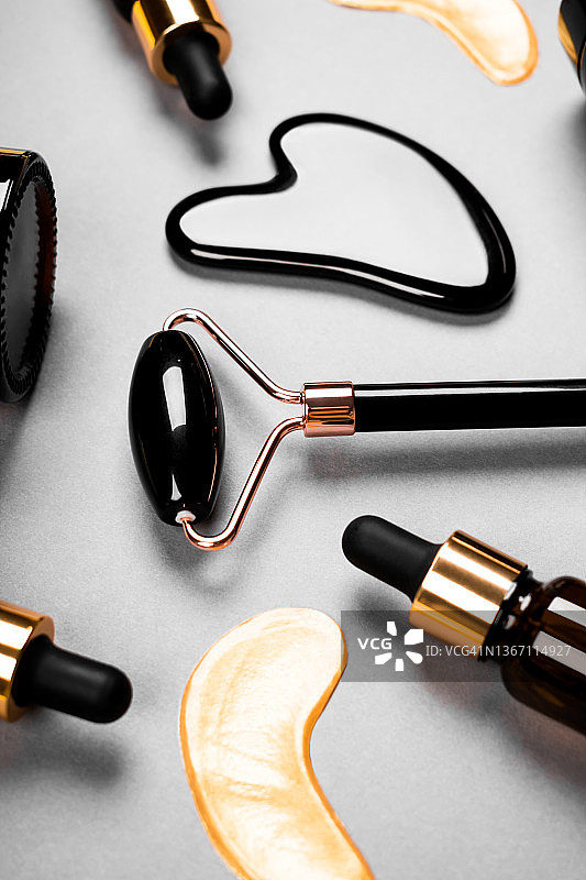 面部按摩器、黑玛瑙面部滚轮、面霜罐和面部精华瓶、抗衰老刮痧按摩、护肤和化妆品竖版概念图片素材