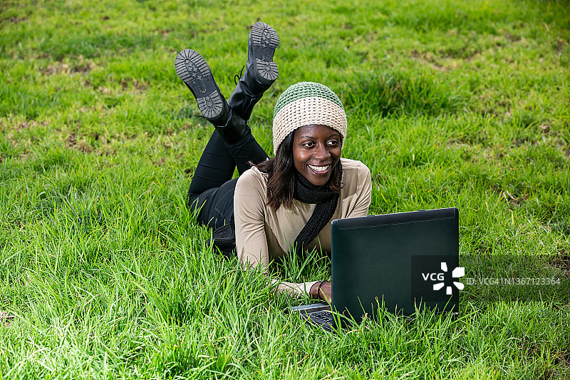 在草地上使用笔记本电脑的快乐黑人女性图片素材