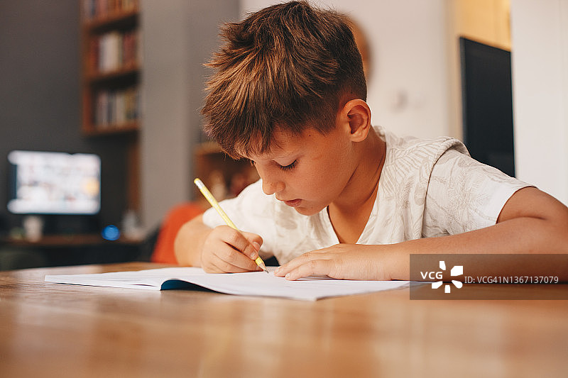 一个用右手写字的孩子坐在桌旁图片素材