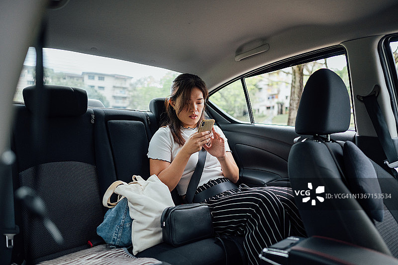 坐在汽车后座上使用智能手机的亚洲女商人图片素材