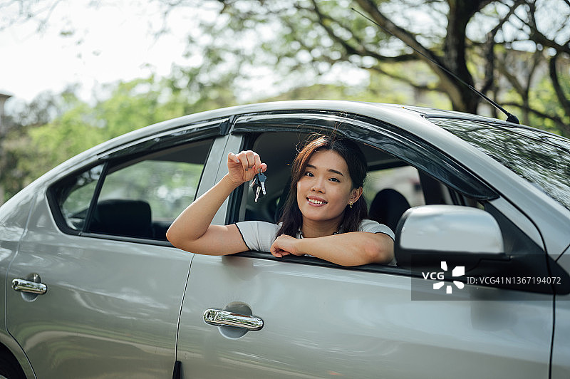 一位有魅力的快乐亚洲女性展示她的新车钥匙图片素材