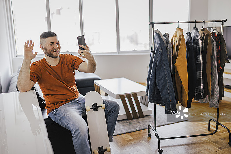 年轻男人在家中用手机自拍，同时挑选衣架上的衣服图片素材