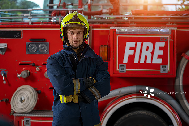 消防员站在消防车旁，手持消防水带，身穿全套防护装备图片素材