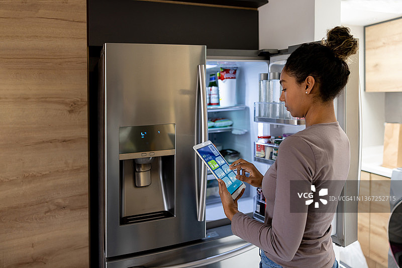女人使用平板电脑上的自动化系统控制冰箱图片素材