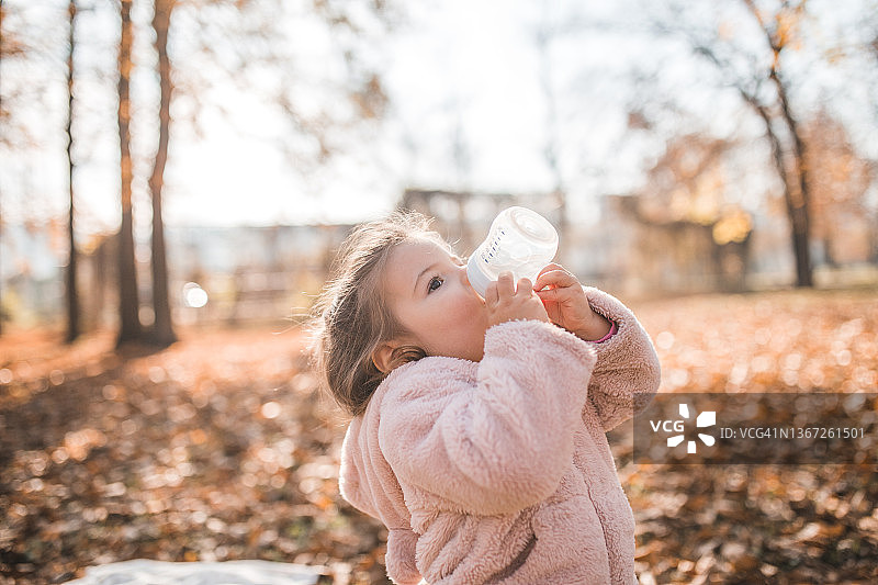 可爱的小女孩在阳光明媚的公园里喝牛奶图片素材