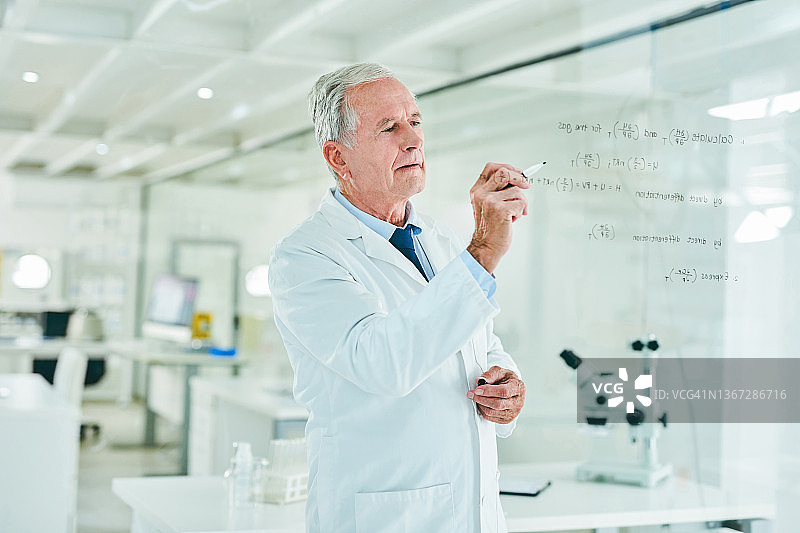 一位资深科学家在实验室的玻璃屏幕上解方程图片素材