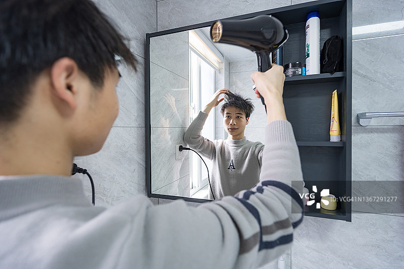 年轻人照镜子，用吹风机吹干头发图片素材