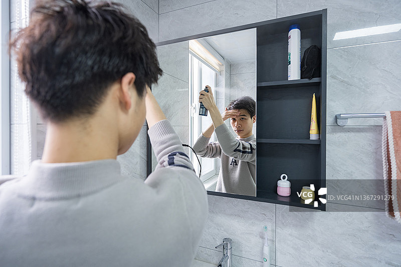 一个年轻男人照镜子并往头发上喷发胶图片素材