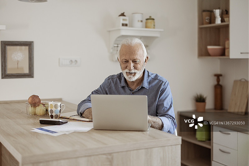 在家中使用笔记本电脑工作的老年男人图片素材