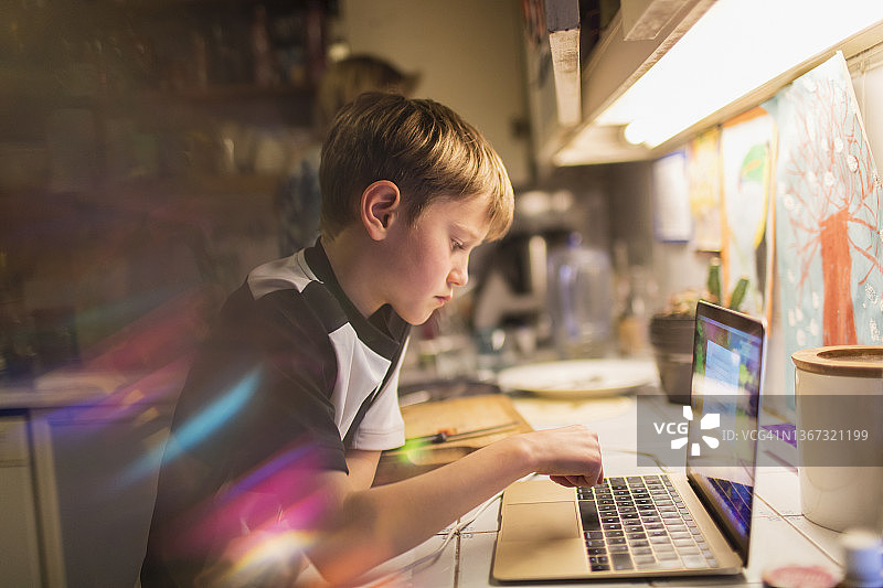 专注的男孩在厨房的笔记本电脑上做作业图片素材