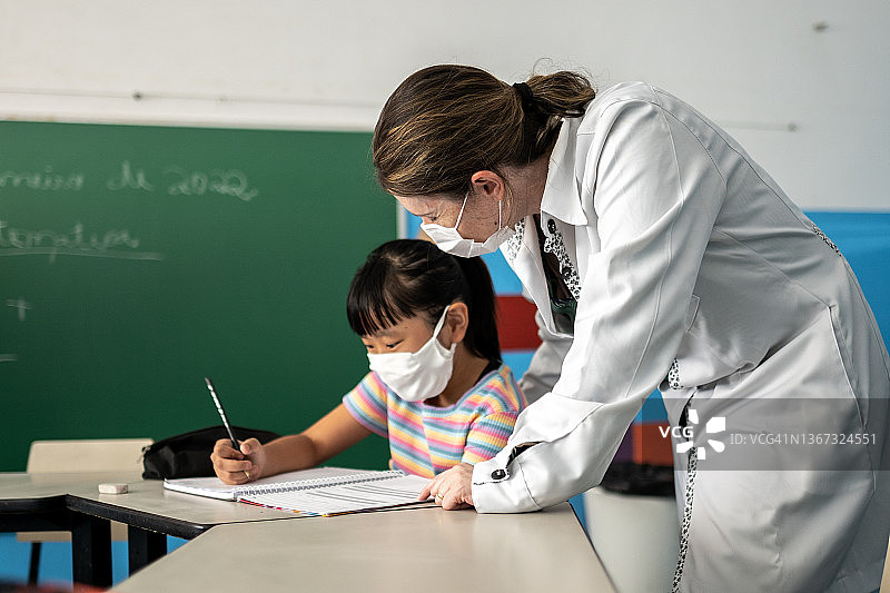 老师在教室里用口罩帮助学生上课图片素材