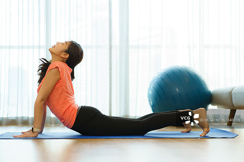 年轻漂亮的亚洲女性在运动服装做瑜伽，而放松在家里的客厅，让锻炼成为她的日常生活，同时保持社交距离。“n图片素材