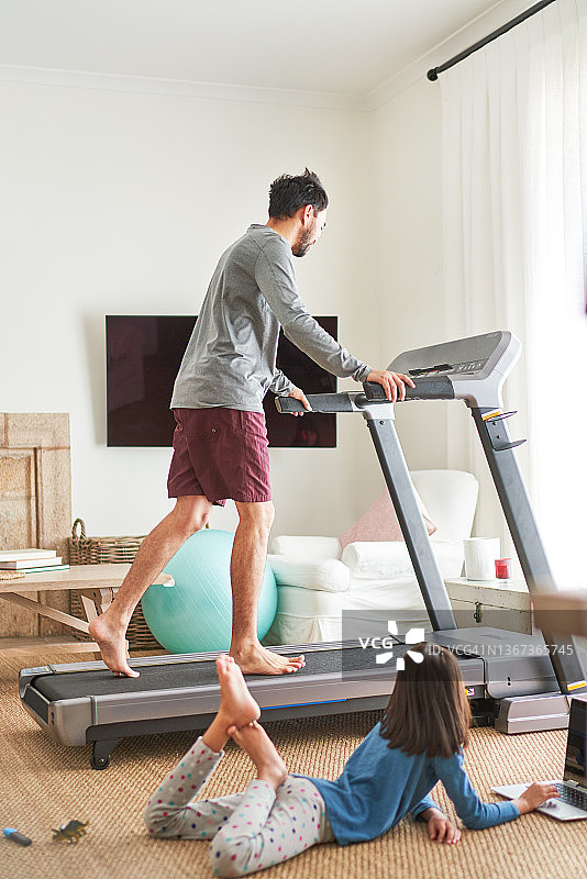 女儿在跑步机上父亲旁边使用笔记本电脑图片素材