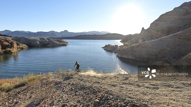 山地自行车骑行者沿着沙漠小路下到湖边图片素材