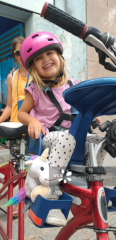戴着自行车头盔，坐在自行车座上微笑的小女孩图片素材
