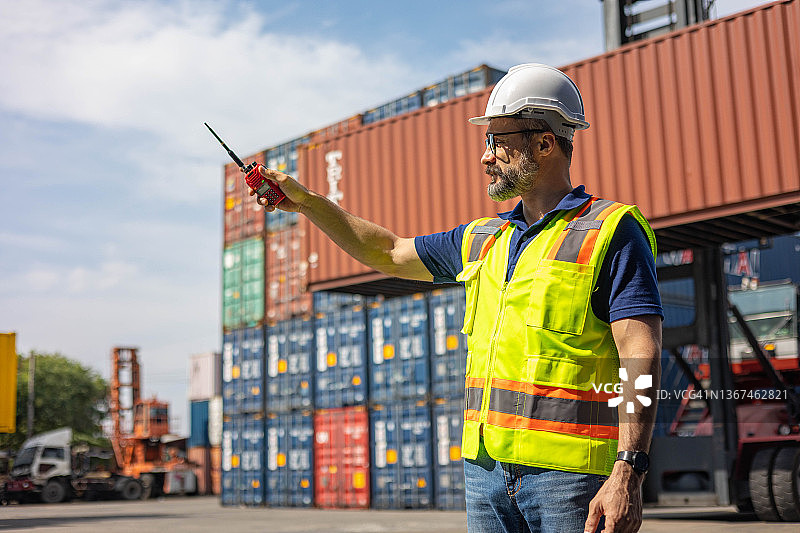 工人在货运集装箱处堆放货物并用对讲机交流图片素材