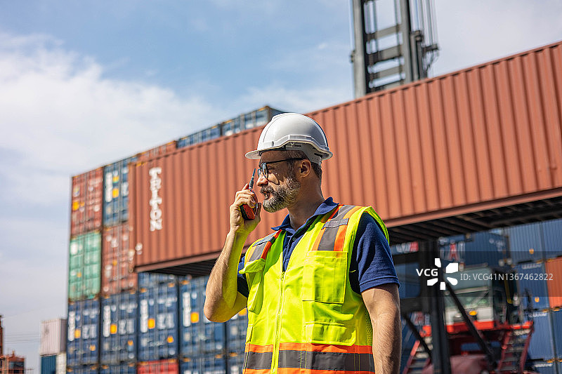 工人在货运集装箱处堆放货物并用对讲机交流图片素材