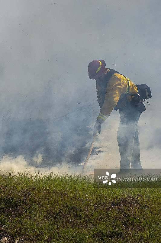 消防员使用工具扑灭冒烟的草火，前景是未燃烧区域图片素材