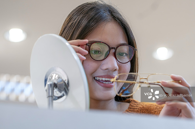 女人在眼镜店拿着眼镜，在眼镜店里挑选新眼镜图片素材
