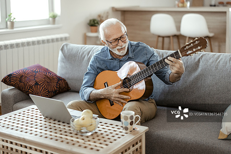 弹吉他并观看在线课程的年长胡须男人图片素材