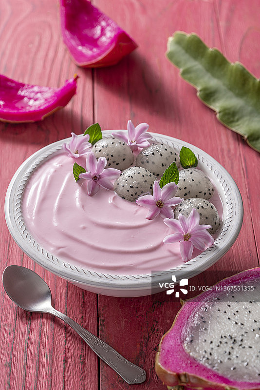 火龙果草莓酸奶早餐碗，薄荷叶，粉色花朵装饰在粉色木桌上图片素材