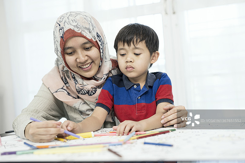 教授创造性问题解决。一位穆斯林母亲正在家中客厅帮助儿子在纸上用蜡笔画画。图片素材
