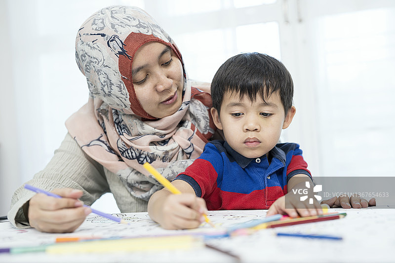 提高手眼协调能力：一位穆斯林母亲在客厅里帮助她的儿子用蜡笔在纸上画画图片素材