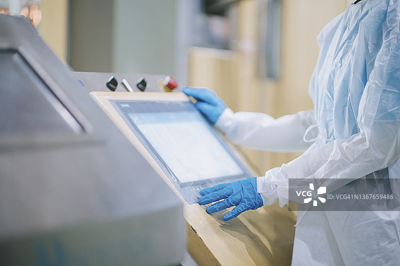 戴着个人防护装备的亚洲华裔女工在生产线上操作瓶装纯净水图片素材