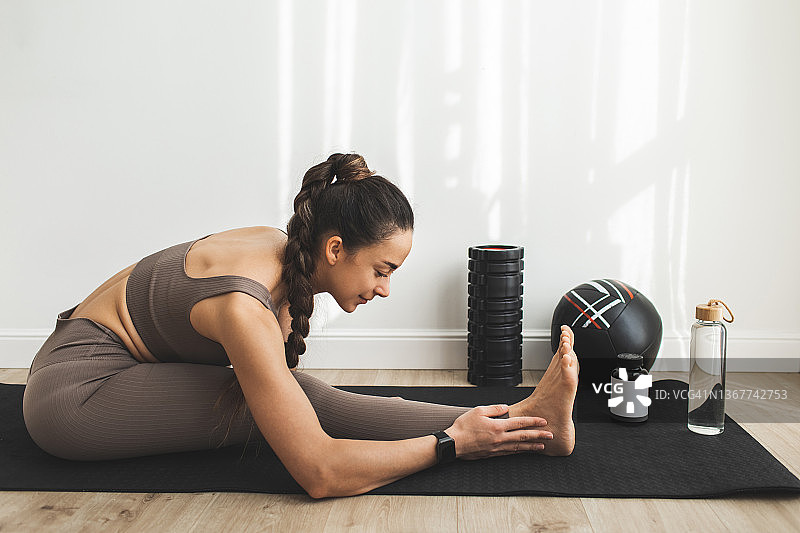 年轻女子在室内垫子上做瑜伽伸展运动图片素材