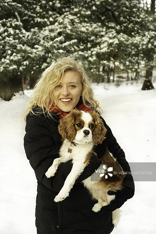 金发女人在雪地里抱着查理士王骑士犬图片素材