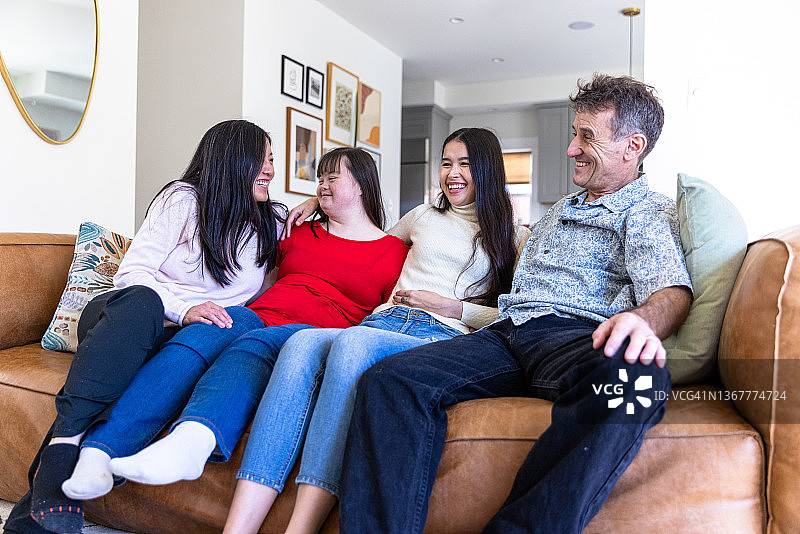 不同肤色的家庭成员一起坐在沙发上，其中一个女儿患有唐氏综合征图片素材
