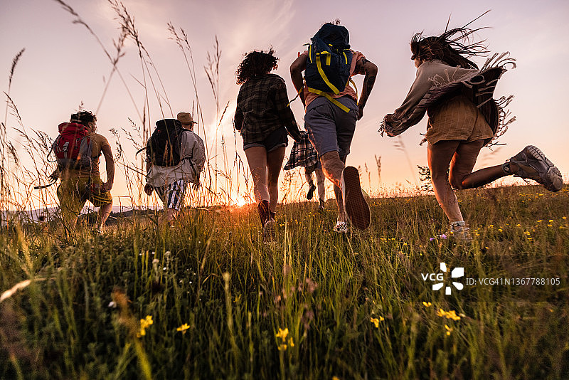 在日落时分在草地上奔跑的无忧无虑的徒步旅行者的背影。图片素材