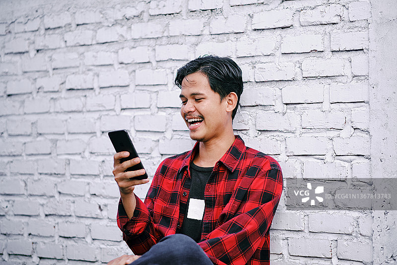 微笑的年轻亚洲男人使用手机访问他的银行图片素材