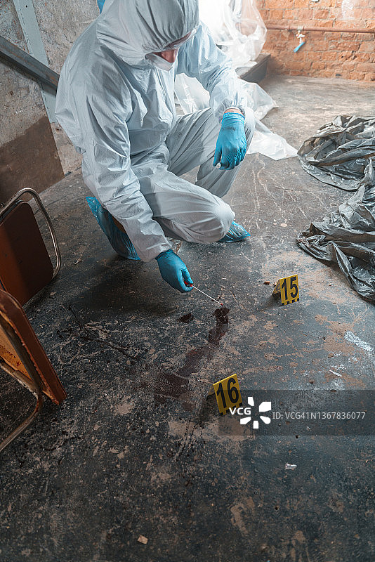 穿防护服的犯罪学家在犯罪现场从地板上提取血样图片素材