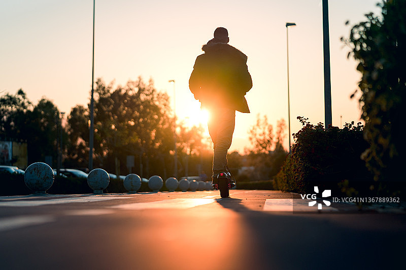 另类通勤：男孩在日落时分使用自行车道上的滑板车图片素材