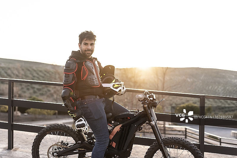 三十多岁男人日落时在观景点与电动摩托车合影图片素材