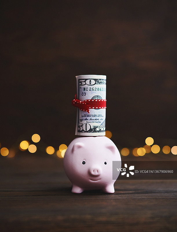 黑暗背景中携带美元纸币卷的粉色小猪储蓄罐：储蓄和金融背景图片素材