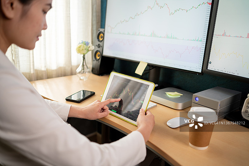 卧室里穿白色西装的亚洲股市投资者正在用电脑和平板查看股票图表图片素材