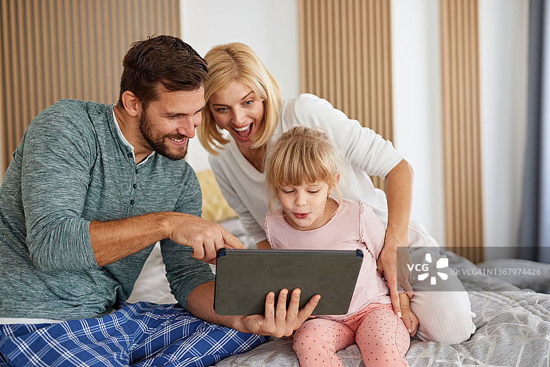 父母和女儿一起看平板电脑上的在线视频，开怀大笑图片素材