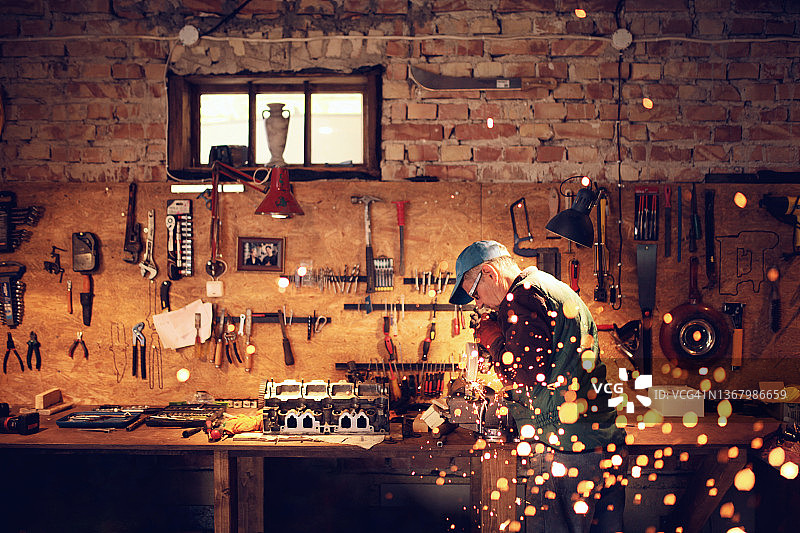 年长的男人在他的工作室用角磨机修理发动机图片素材