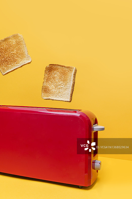 黄色背景上的红色烤面包机和两片面包图片素材