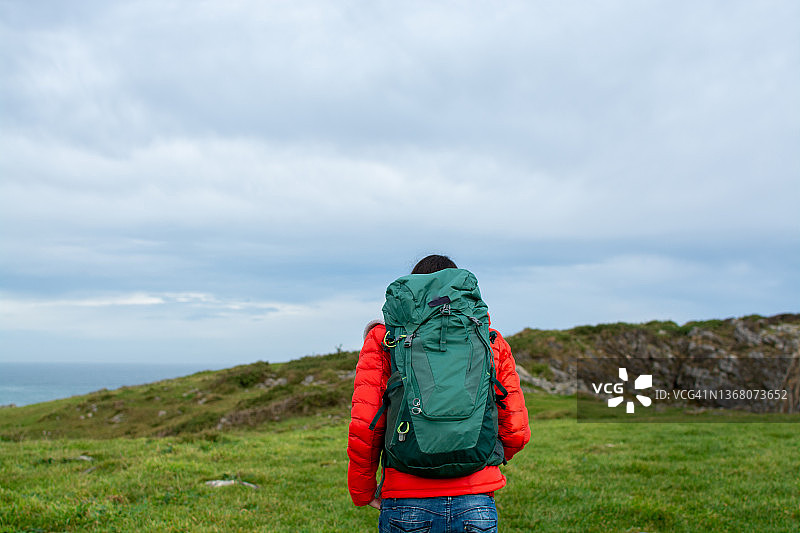 阴天里沿着悬崖行走的背包女子背影图片素材