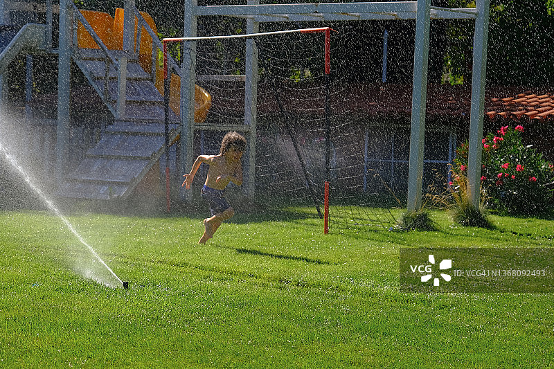 孩子们在后院草坪上玩洒水器，享受水乐趣图片素材