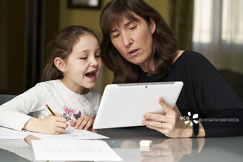 母亲在家辅导女儿用平板电脑完成学校作业图片素材