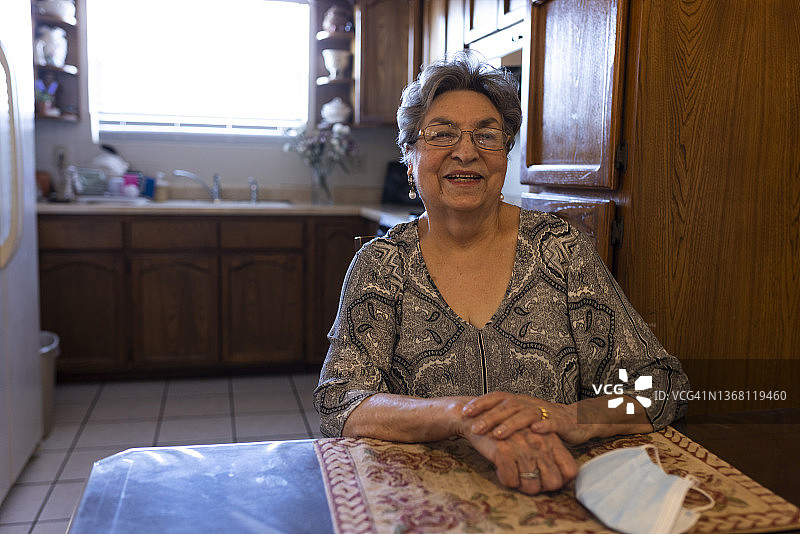 快乐的老年妇女坐在厨房里，桌子上放着防护口罩图片素材