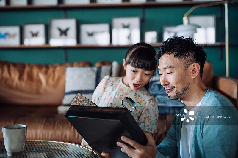 年轻的亚裔父亲和可爱的女儿在家一起用放大镜检查昆虫标本收藏。分享共同的爱好。爱好和兴趣概念图片素材