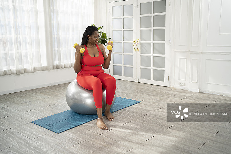 在家使用健身球和哑铃锻炼的年轻女人图片素材